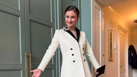 Uma mulher com cabelo cacheado e vestido verde est sorrindo para a cmera. O fundo mostra vrias pessoas, algumas com cmeras, em um evento que parece ser uma gala ou tapete vermelho, com decorao de plantas ao redor. Chloe Malle trabalha h 14 anos na r