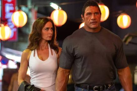 A imagem mostra um casal caminhando em uma rua iluminada por lanternas. A mulher est vestindo um vestido branco e tem cabelo solto, enquanto o homem, que  musculoso, usa uma camiseta cinza e jeans. Eles parecem estar em um ambiente noturno, com luzes col