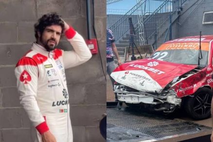 Homem vestido com macaco branco e vermelho de piloto de corrida est encostado em parede de blocos de concreto, com a mo na cabea. Ao lado, carro de corrida vermelho e branco com nmero 92 apresenta danos graves na parte frontal, sendo transportado em p