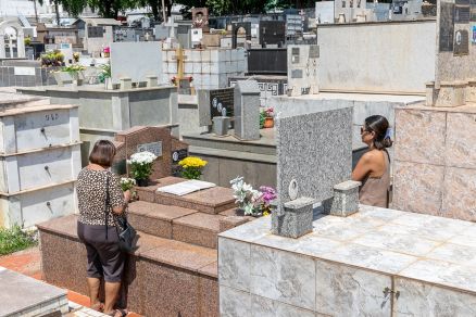 Familiares em visita ao cemitrio; duas mulheres prximas a um tmulo em orao